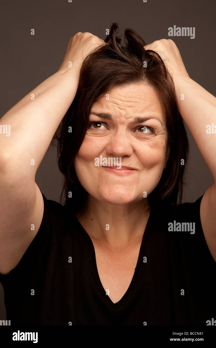 A thirty year old adult woman tearing at her long brown hair in anger and frustration Stock Photo