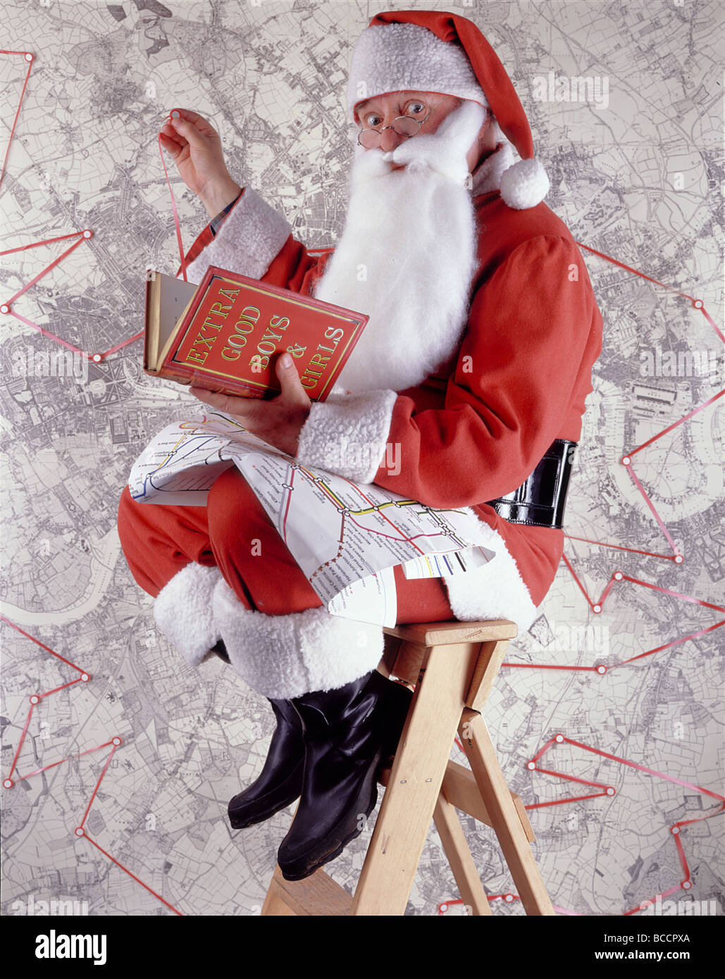 Santa Claus (or Father Christmas) against map and with book entitled ‘EXTRA GOOD BOYS & GIRLS’ Stock Photo