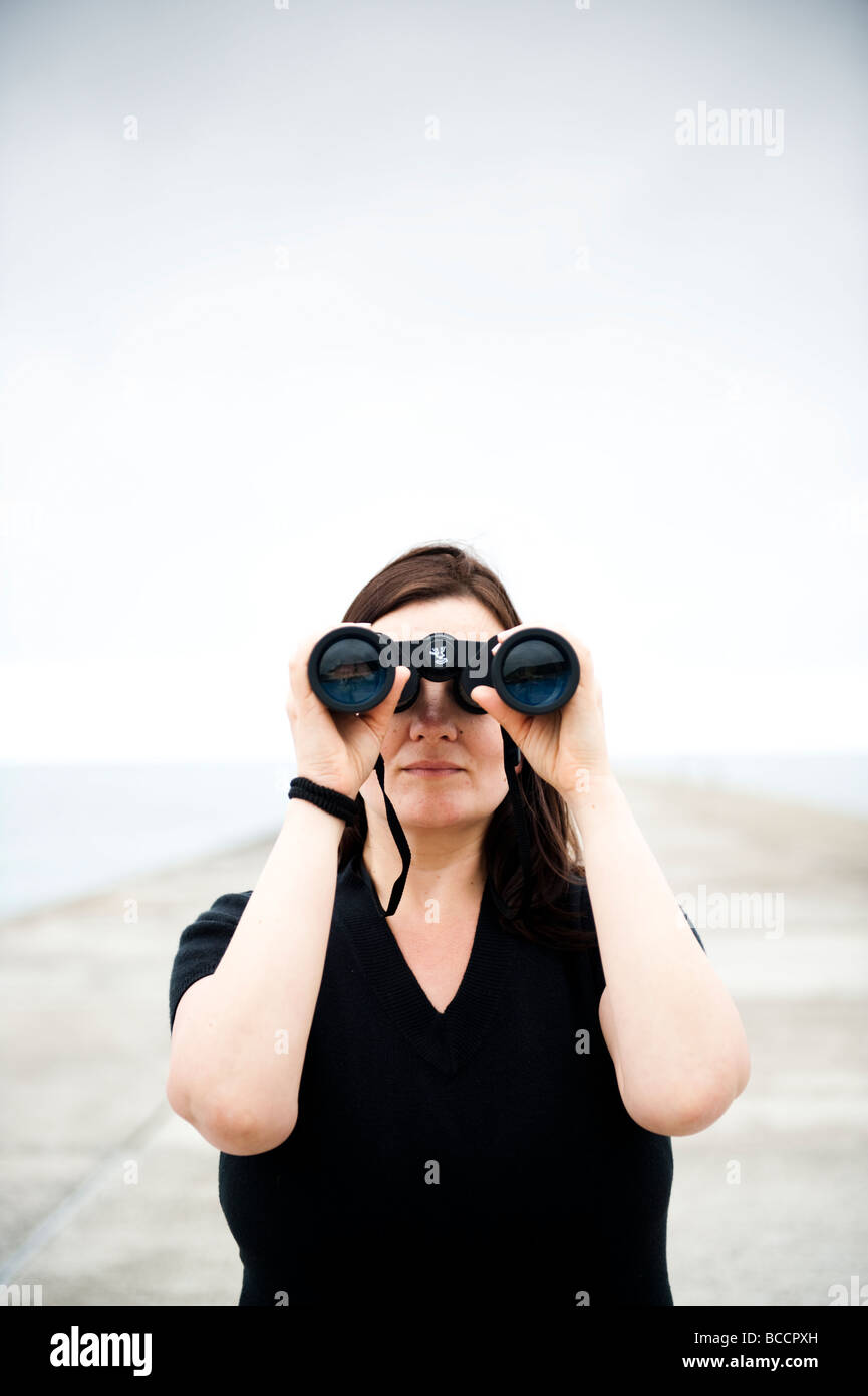 A woman looking through a pair of binoculars - observing spying on stalking spy following seeing close up Stock Photo