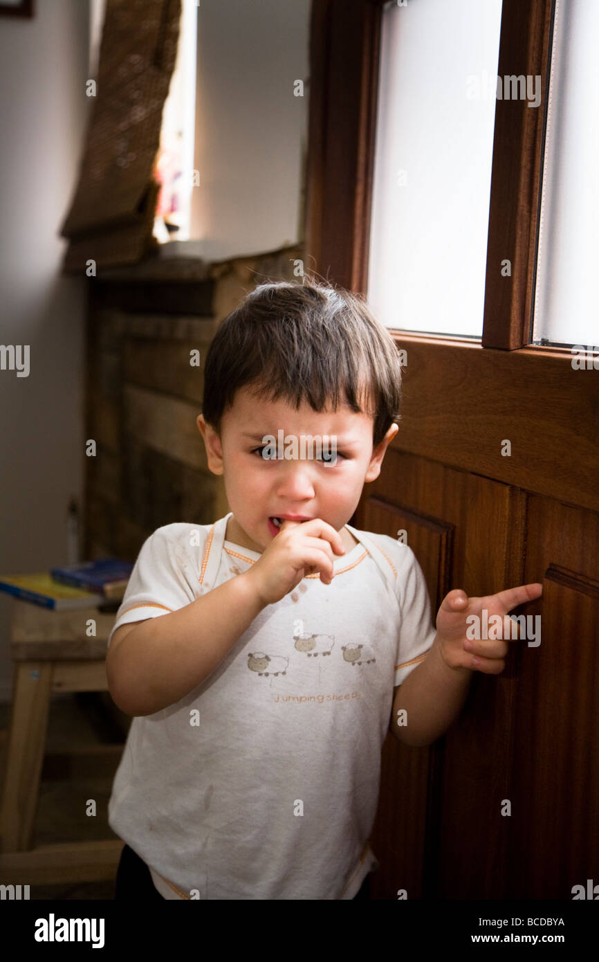 Young boy waiting by the door at home, crying for his mum. Stock Photo