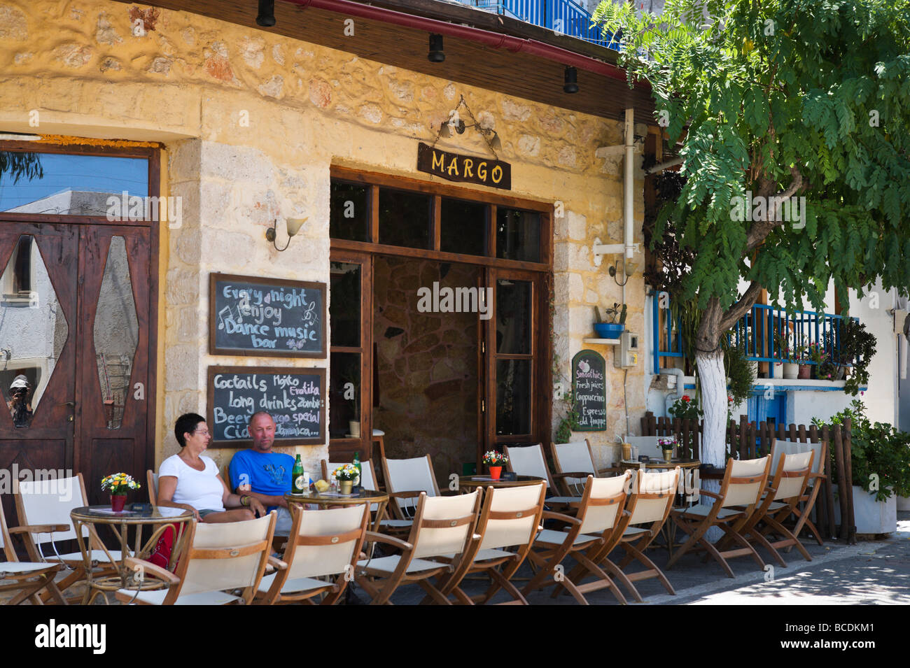 Couple sitting outside a bar on the main street in Old Hersonissos Village,  North Coast, Crete, Greece Stock Photo - Alamy