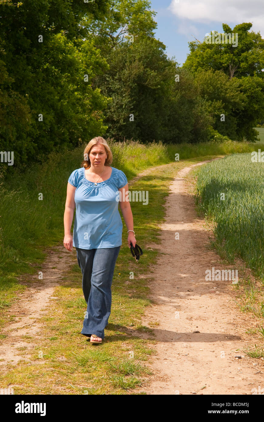 A woman in her thirties walking alone down a country farm track in the uk countryside in spring Stock Photo