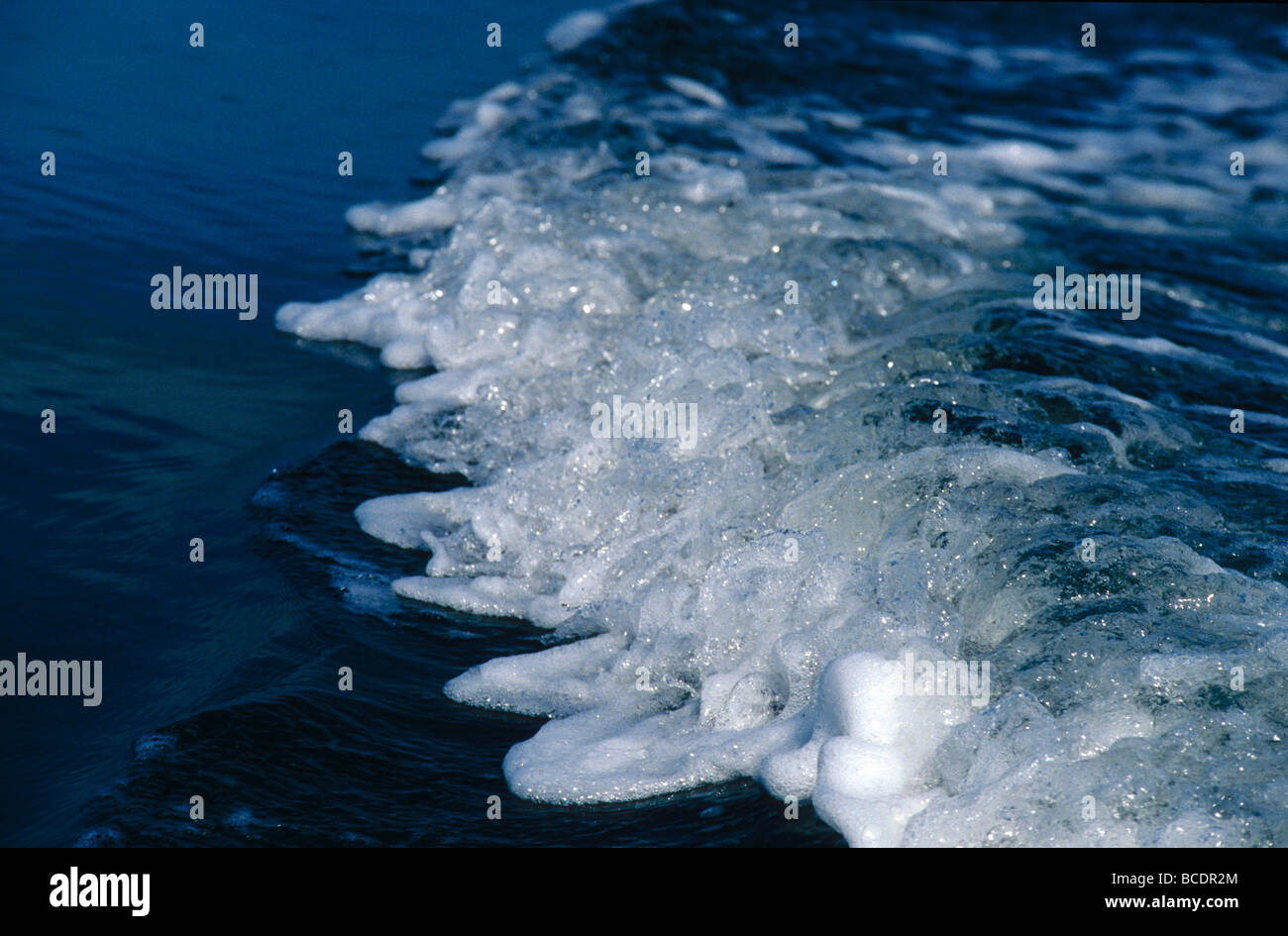 A white foamy motor boat wake pulses on a still lake surface. Stock Photo