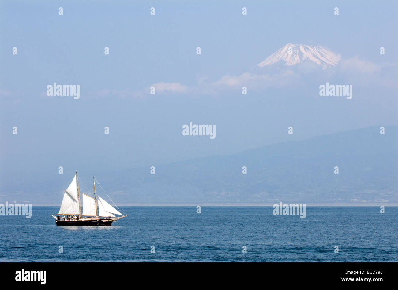 A schooner sailboat on the Pacific Ocean slowly passing a partially obscured Mount Fuji near Numazu Japan Stock Photo