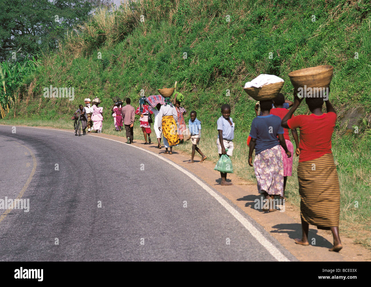 Local people and barefoot women carrying head loads along road side to market near Kabale south west Uganda East Africa Stock Photo