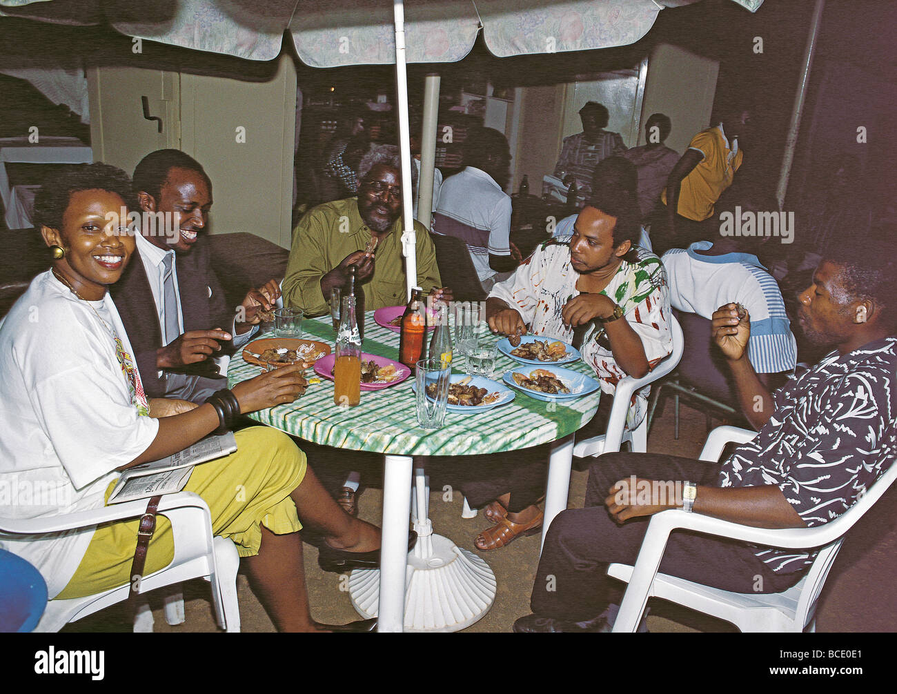 Mixed group of young African men and women enjoy Nyama choma roast meat at roadside cafe Kampala Uganda East Africa Stock Photo