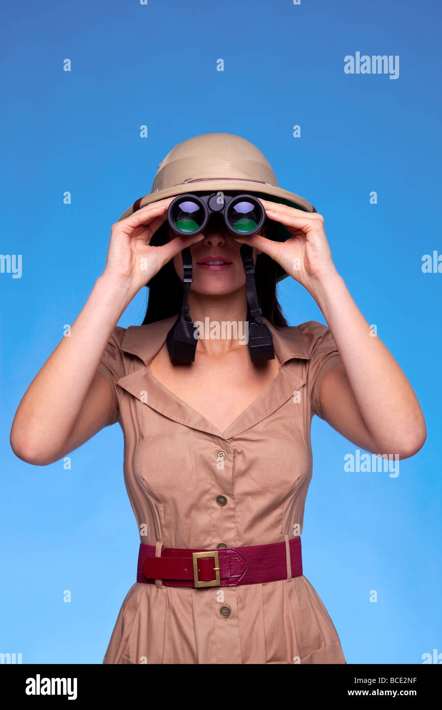 A woman wearing a pith helmet searching with a pair of binoculars blue background with copy space Stock Photo