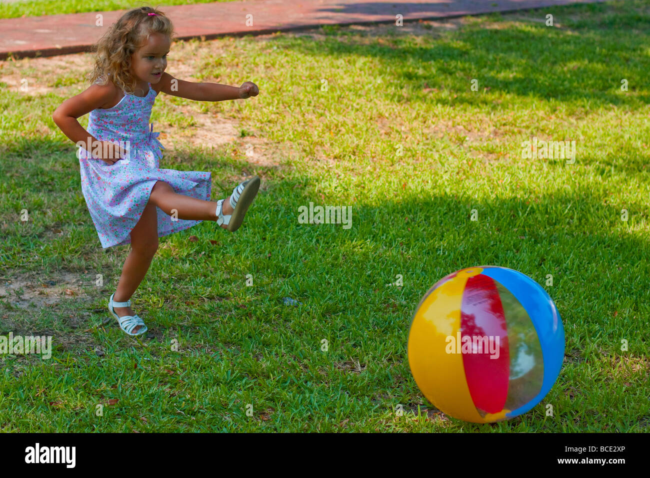 Kickball. Cute little blond girl in dress running and kicking beach
