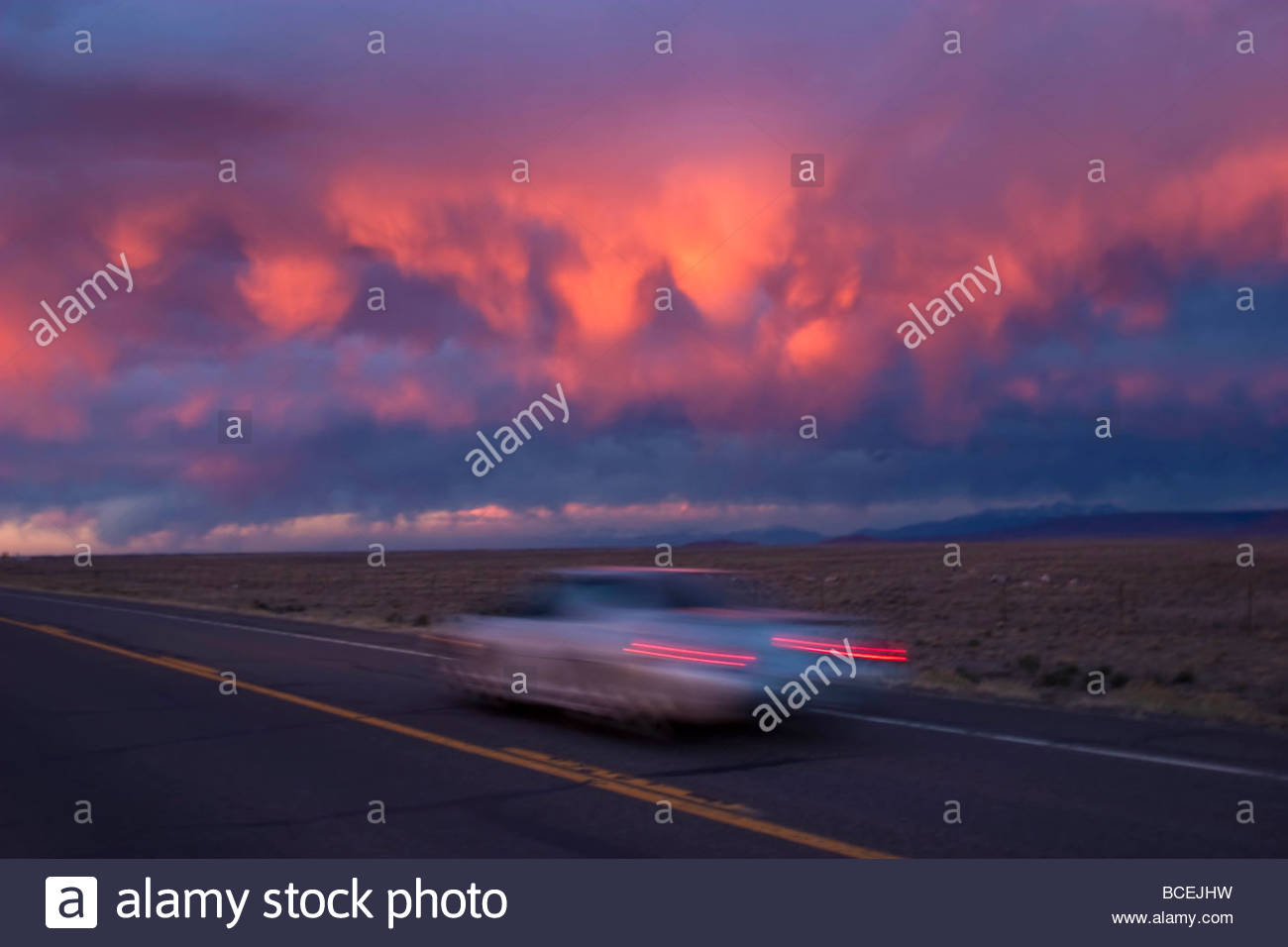 A vintage car drives along a vacant road in Taos, New Mexico. Stock Photo