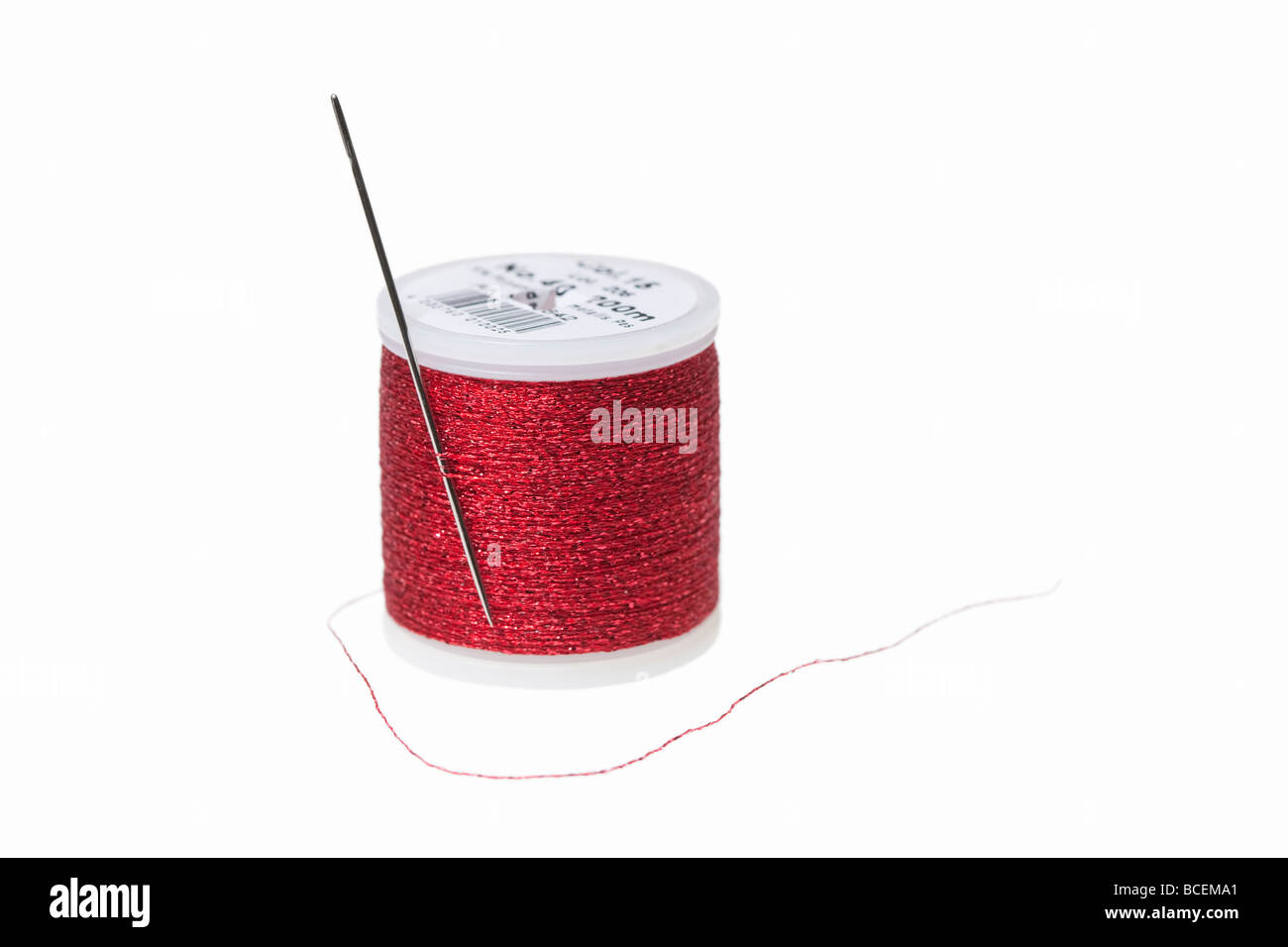 Sewing needle and a reel of metallic red thread against a white background Stock Photo