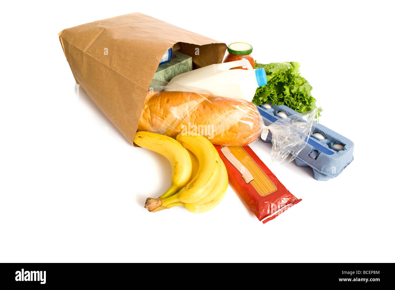 A brown paper bag full of groceries on a white background with bread