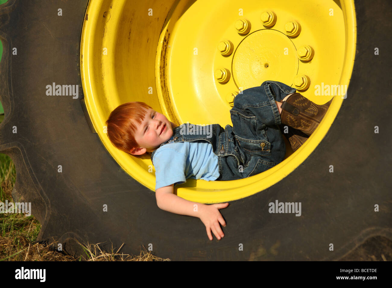 Young boy laying in large tractor wheel Stock Photo