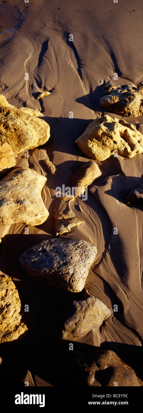 Waves leave beautiful patterns trailing behind boulders on a beach. Stock Photo