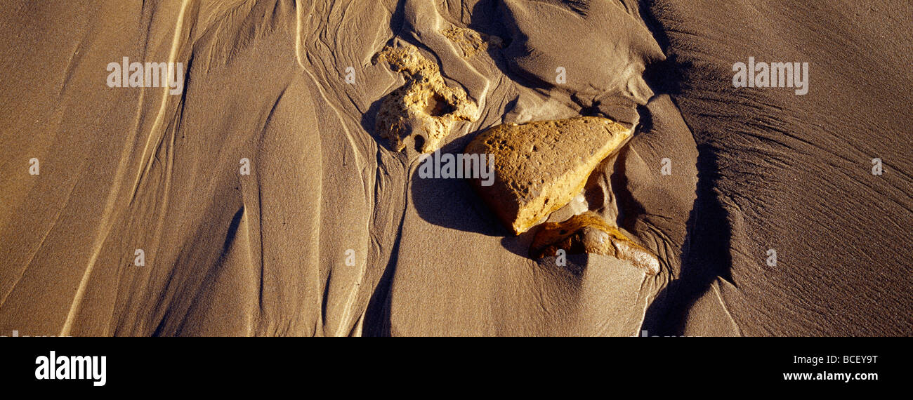 Waves leave beautiful patterns trailing behind boulders on a beach. Stock Photo