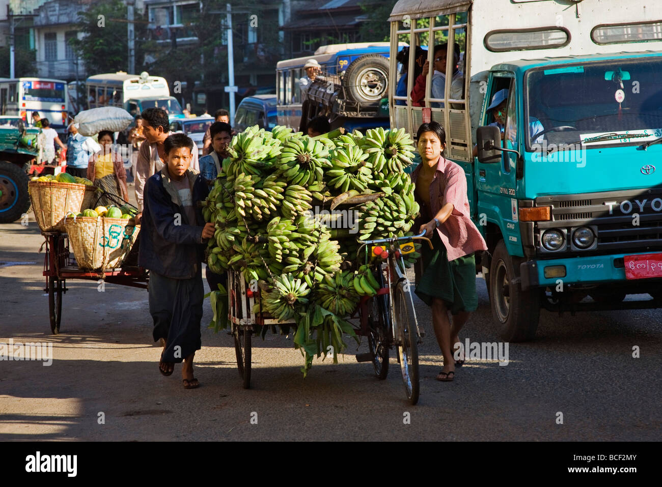 Myanmar, Burma, Yangon. A busy street scene in Yangon with trishaws laden with fruit heading for market. Stock Photo