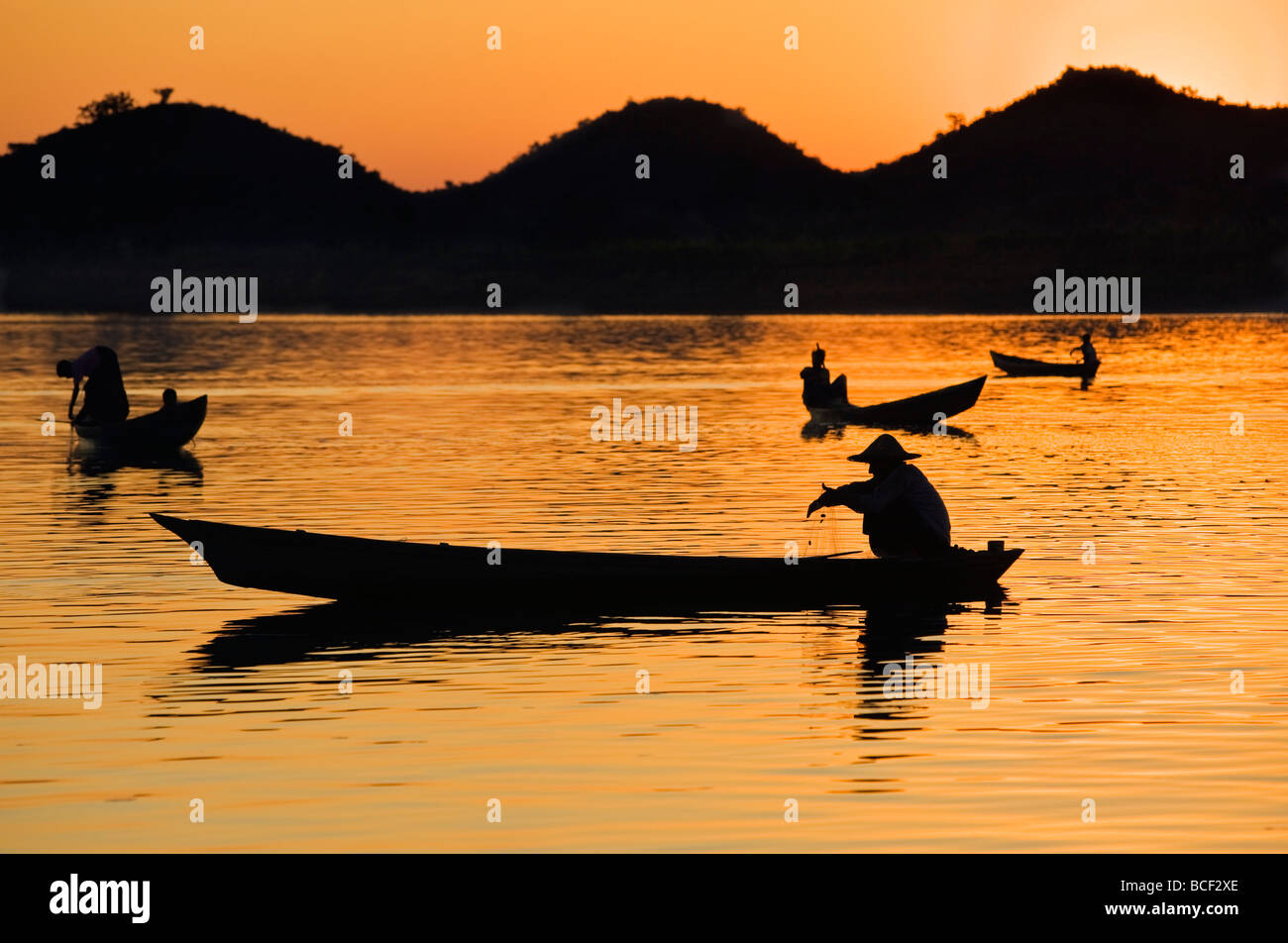 Fishermen bathed in the golden hues of the setting sun as they fish from their little boats on the Lay Myo River. Stock Photo