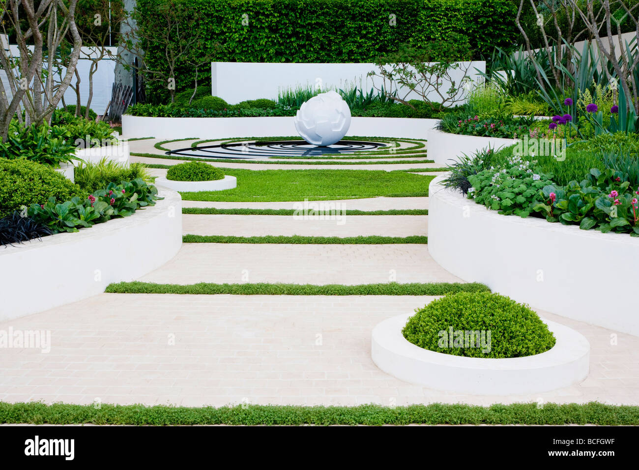 White globe sculpture in water rings with white paving and walls with raised beds Stock Photo