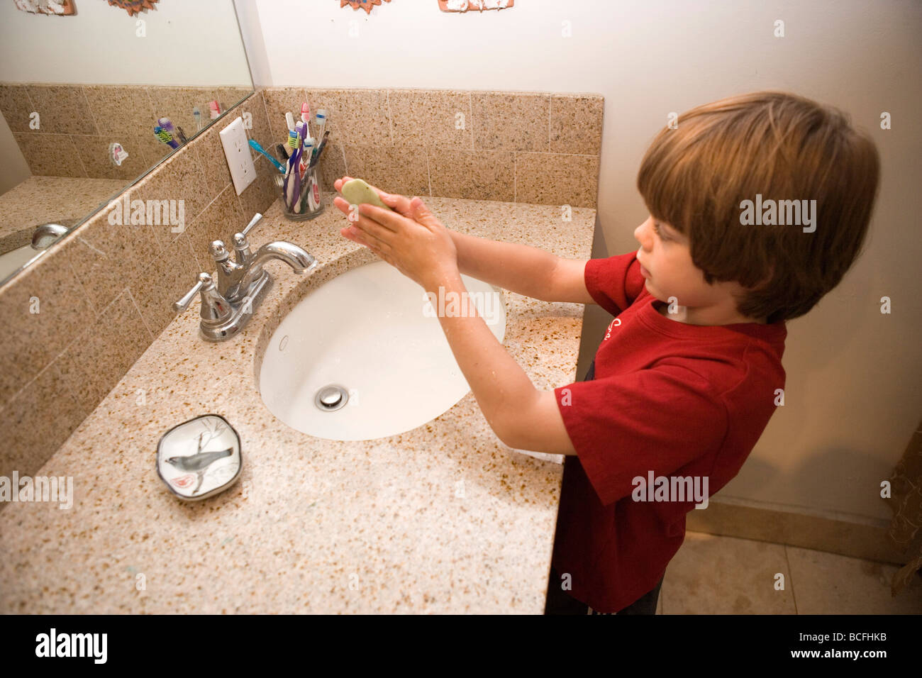 a seven year old boy washing his hands with soap in the bathroom sink at home Stock Photo
