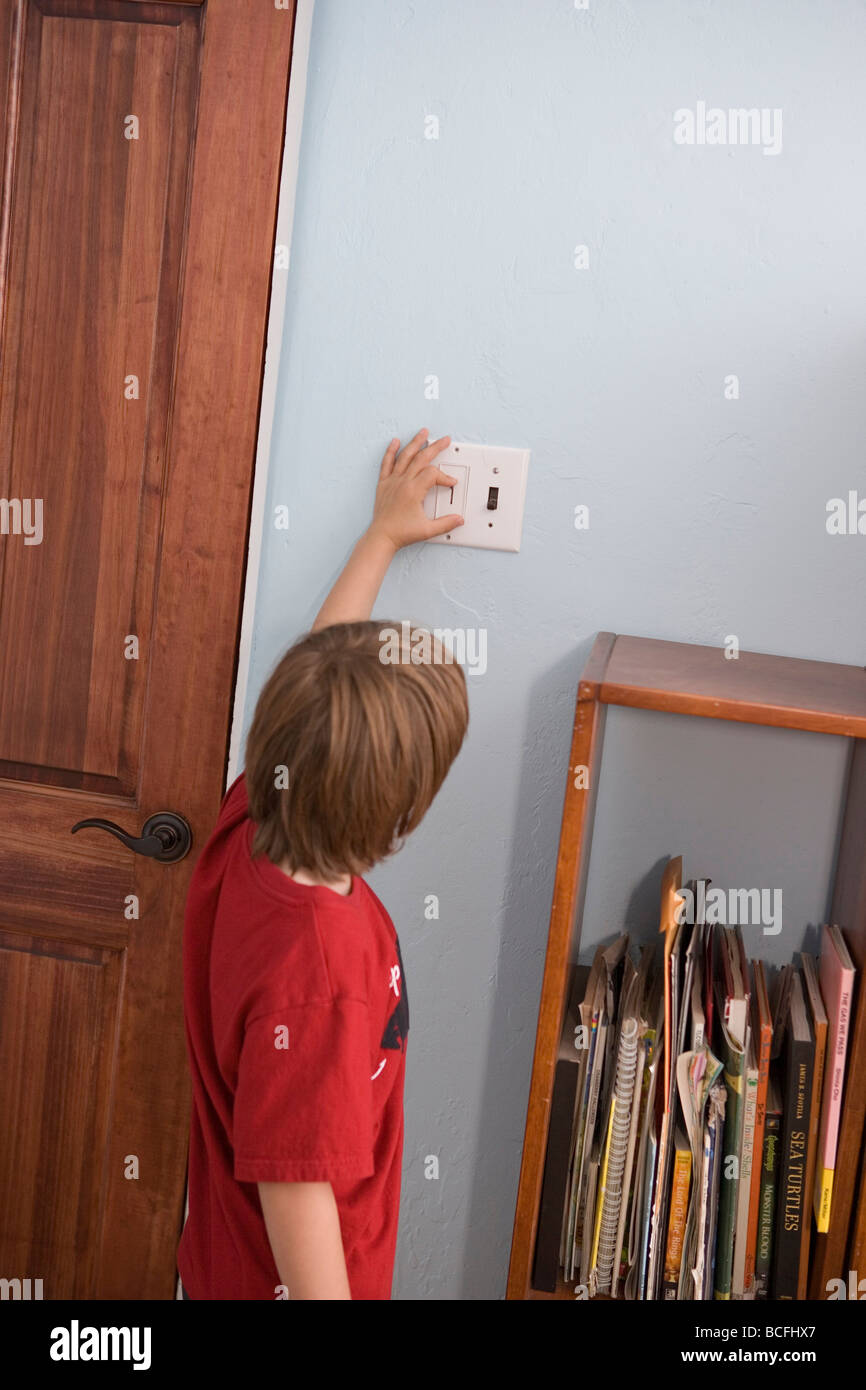 seven year old boy turning off and on light switch in his bedroom Stock Photo