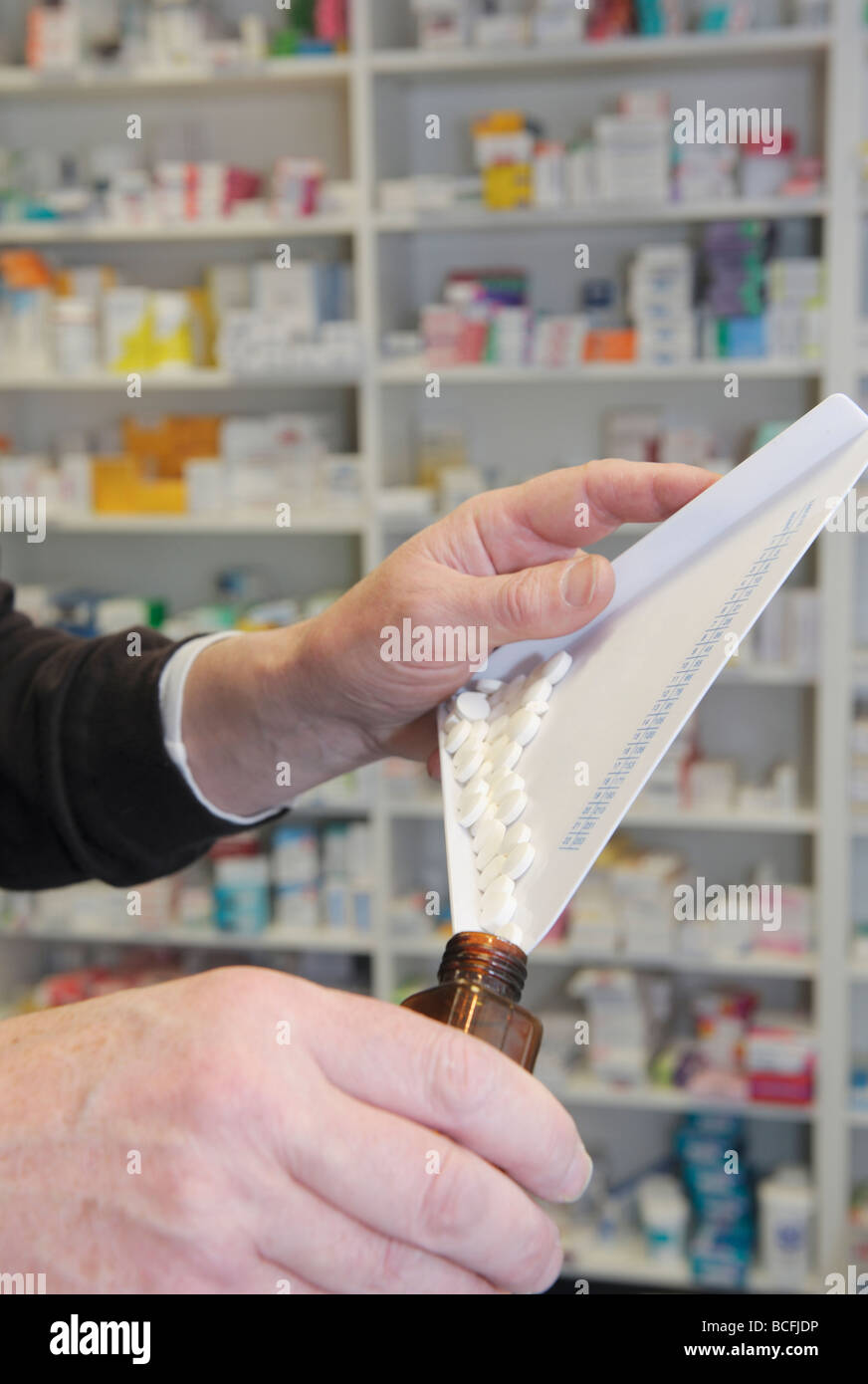 Chemist dispensing pills into a brown bottle with his hands Stock Photo
