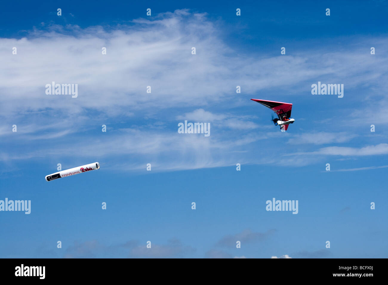 Photograph of Ultralight trike with condoms advertisements on its wing, and its back, flying on intense blue sky. Stock Photo