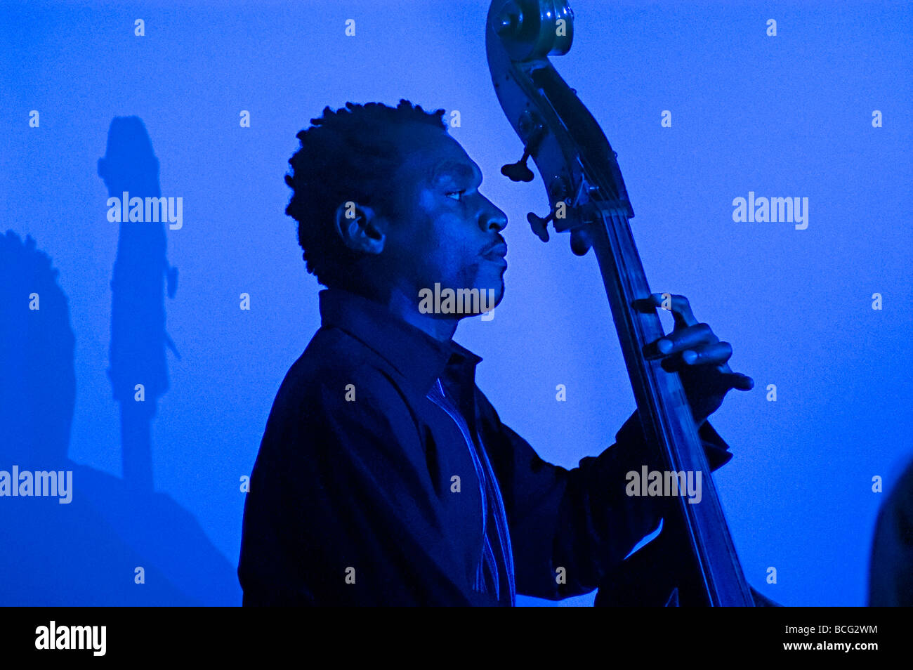 a black double bass player with shadow behind him bathed in blue light