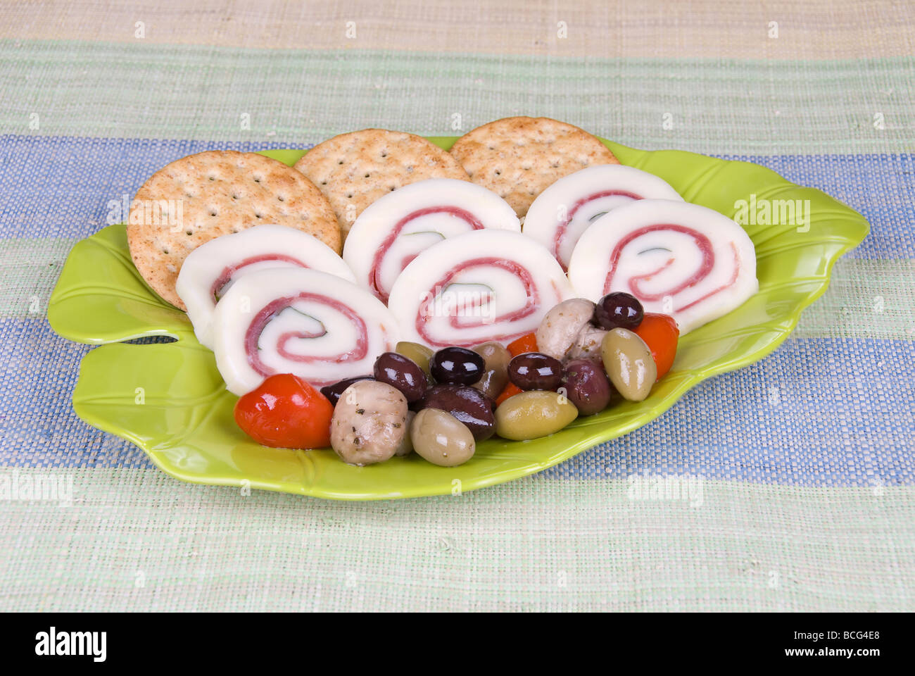 A yummy snack plate of prosciutto ham basil cheese rolls with an olive assortment and crackers Stock Photo