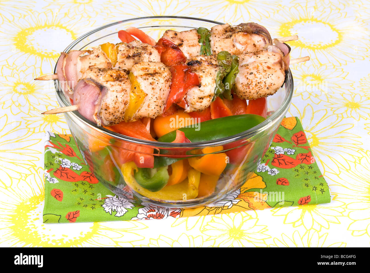 Freshly barbecued skewers of chicken kebobs with bell peppers and onions on a bowl of fresh bell peppers for snacking Stock Photo