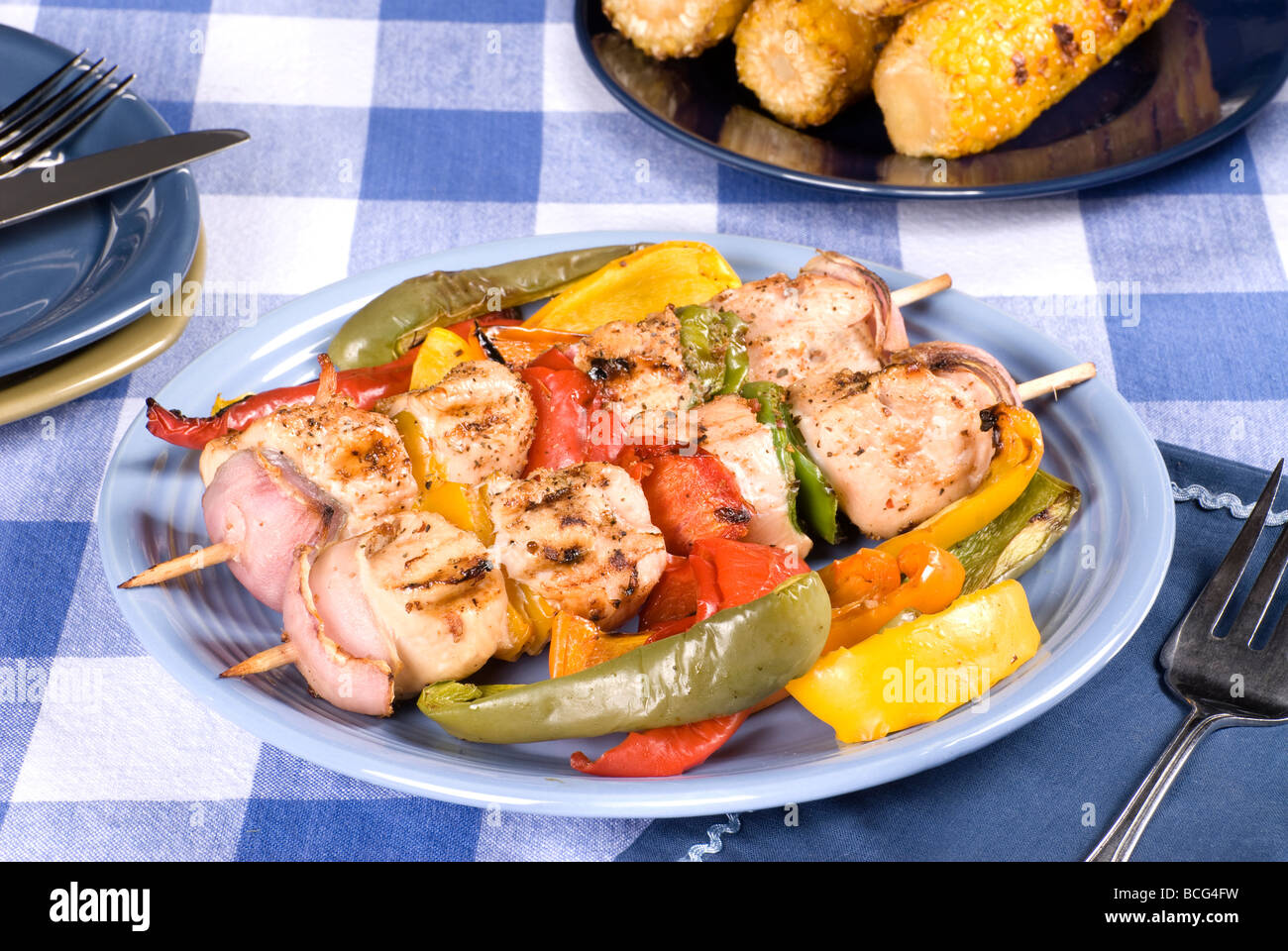 A barbecued chicken kebab dinner with corn on the cob on a picnic table setting Stock Photo