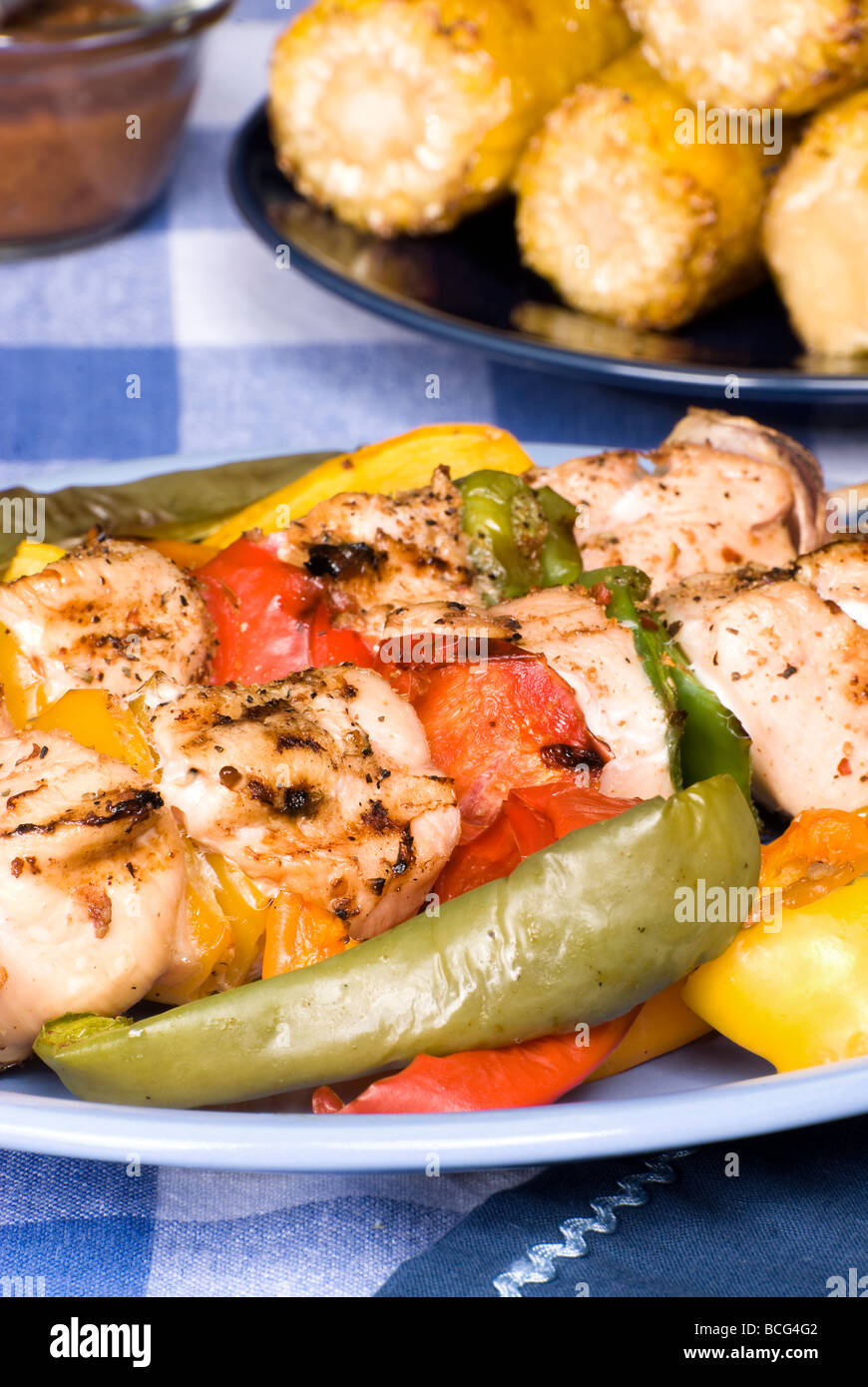 A barbecued chicken kebab dinner with corn on the cob on a picnic table setting Stock Photo