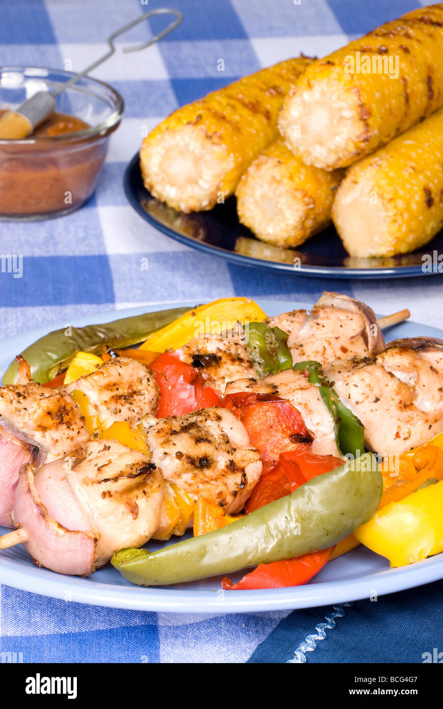A barbecued chicken kebob dinner with corn on the cob on a picnic table setting Stock Photo