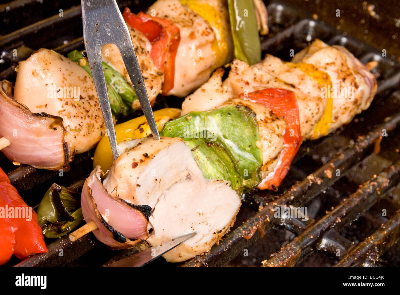 Grilled barbecued chicken kebob being cut open to see if it is ready to eat Stock Photo