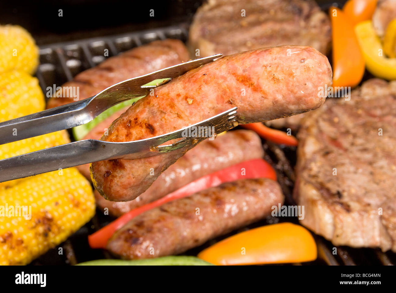 A beer bratwurst on a barbecue being rotated for maximum flavor Stock Photo