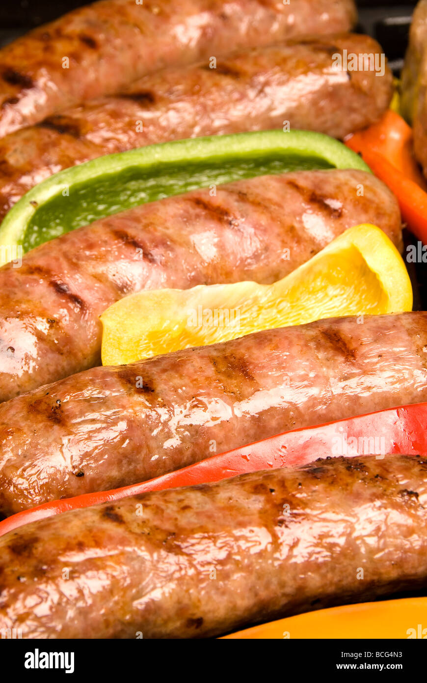 A row of grilled barbecued bratwurst with bell pepper garnish ready to serve Stock Photo