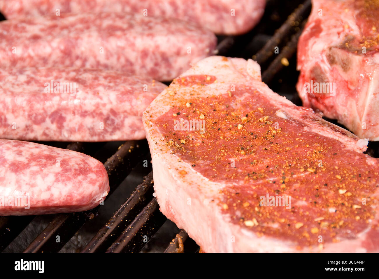Raw steaks and bratwurst on a barbecue grill ready to be cooked Stock Photo