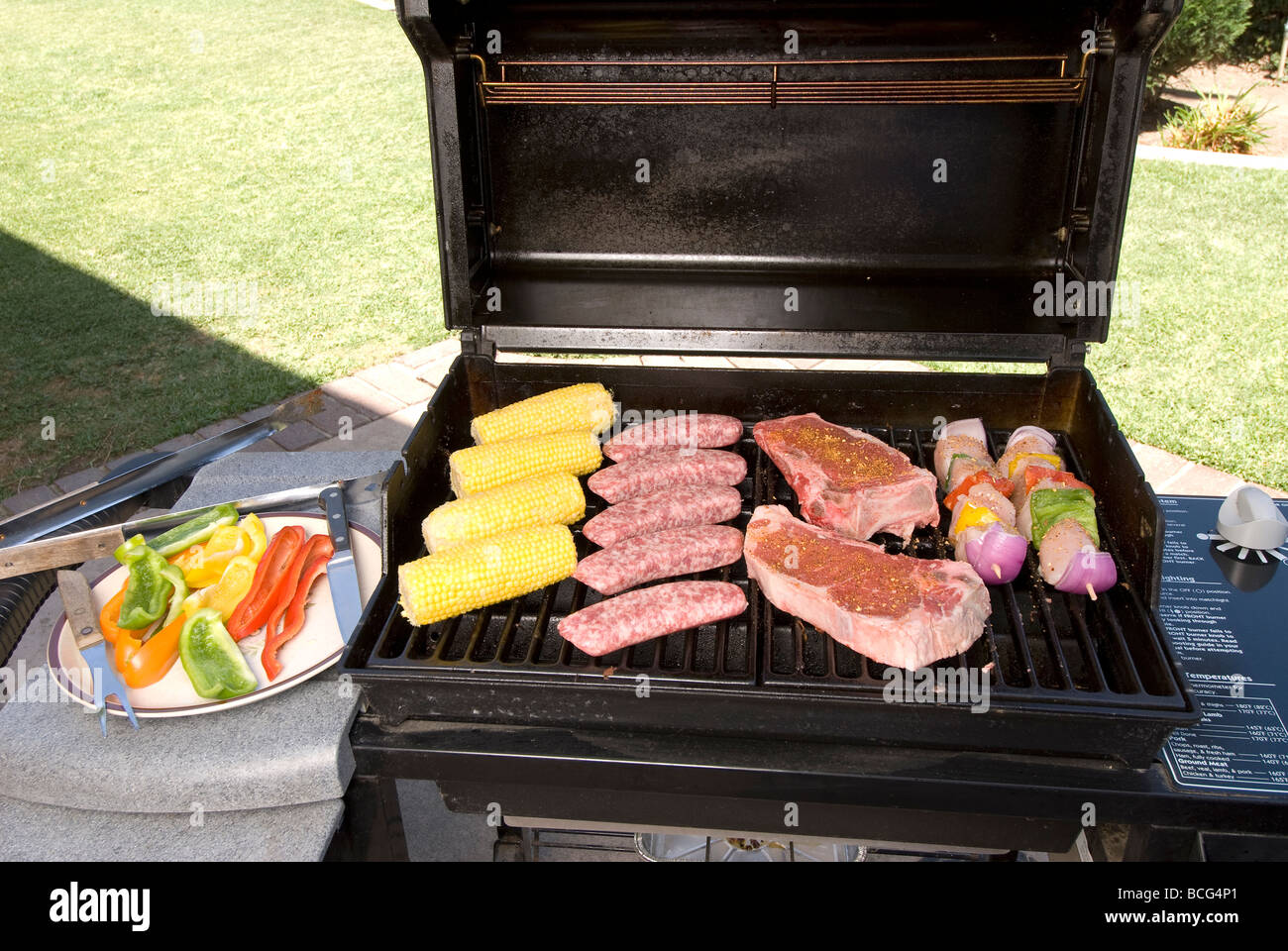 A barbecue prepared to cook corn on the cob steak bratwurst and chicken kebabs Stock Photo