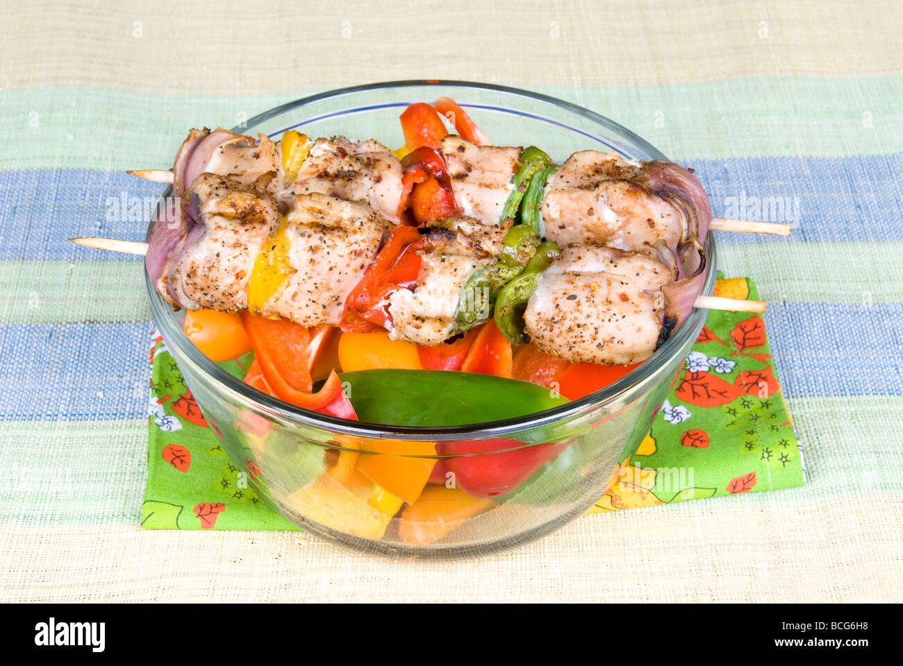 Freshly barbecued skewers of chicken kebobs with bell peppers and onions on a bowl of fresh bell peppers for snacking Stock Photo