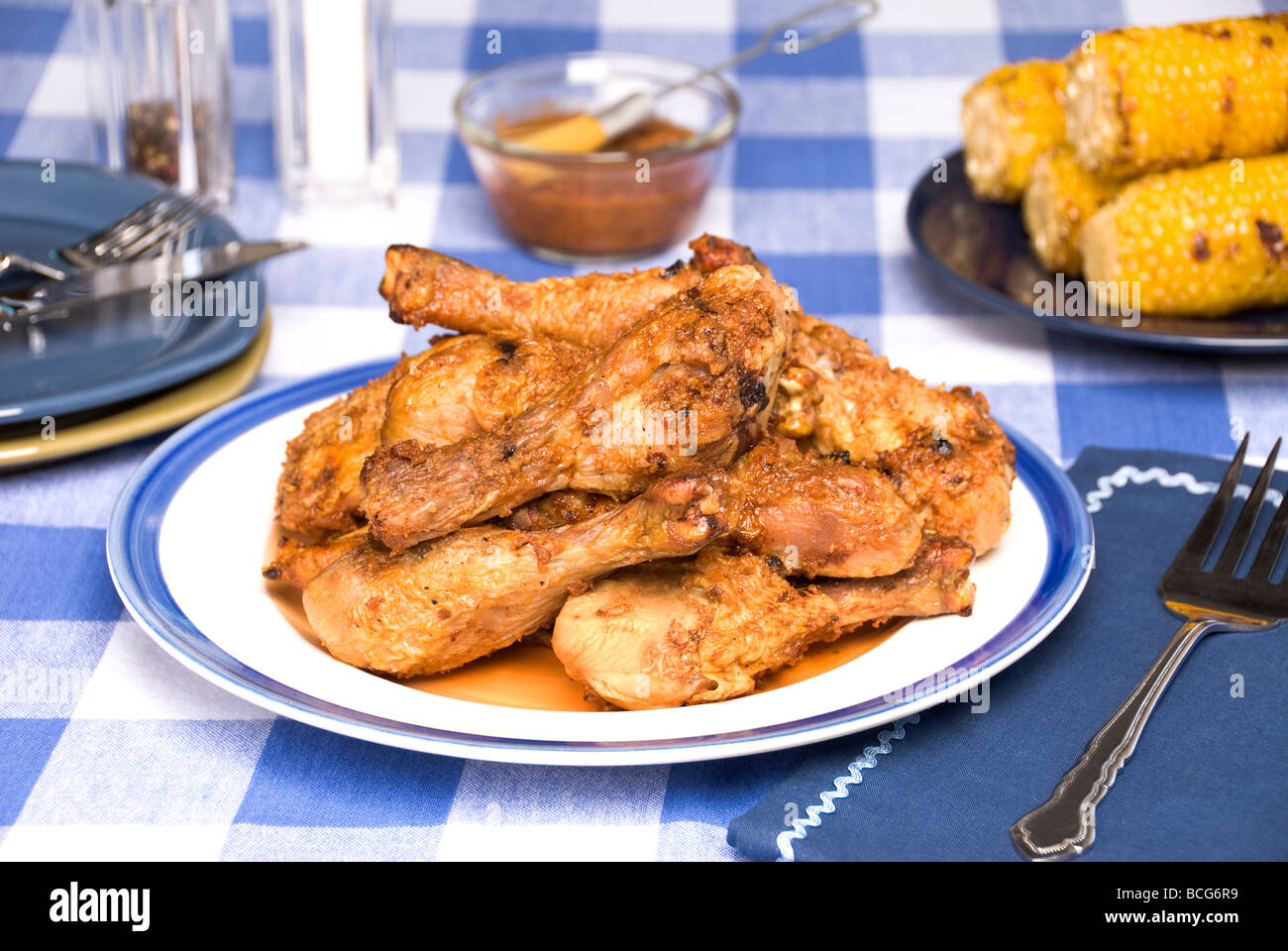 A plate of barbecued chicken drum legs on a picnic table with corn on the cob vegetables in the background Stock Photo