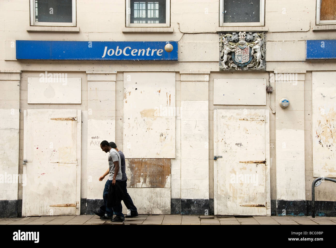 Shoreditch Closed and boarded up job centre with two men walking past Stock Photo