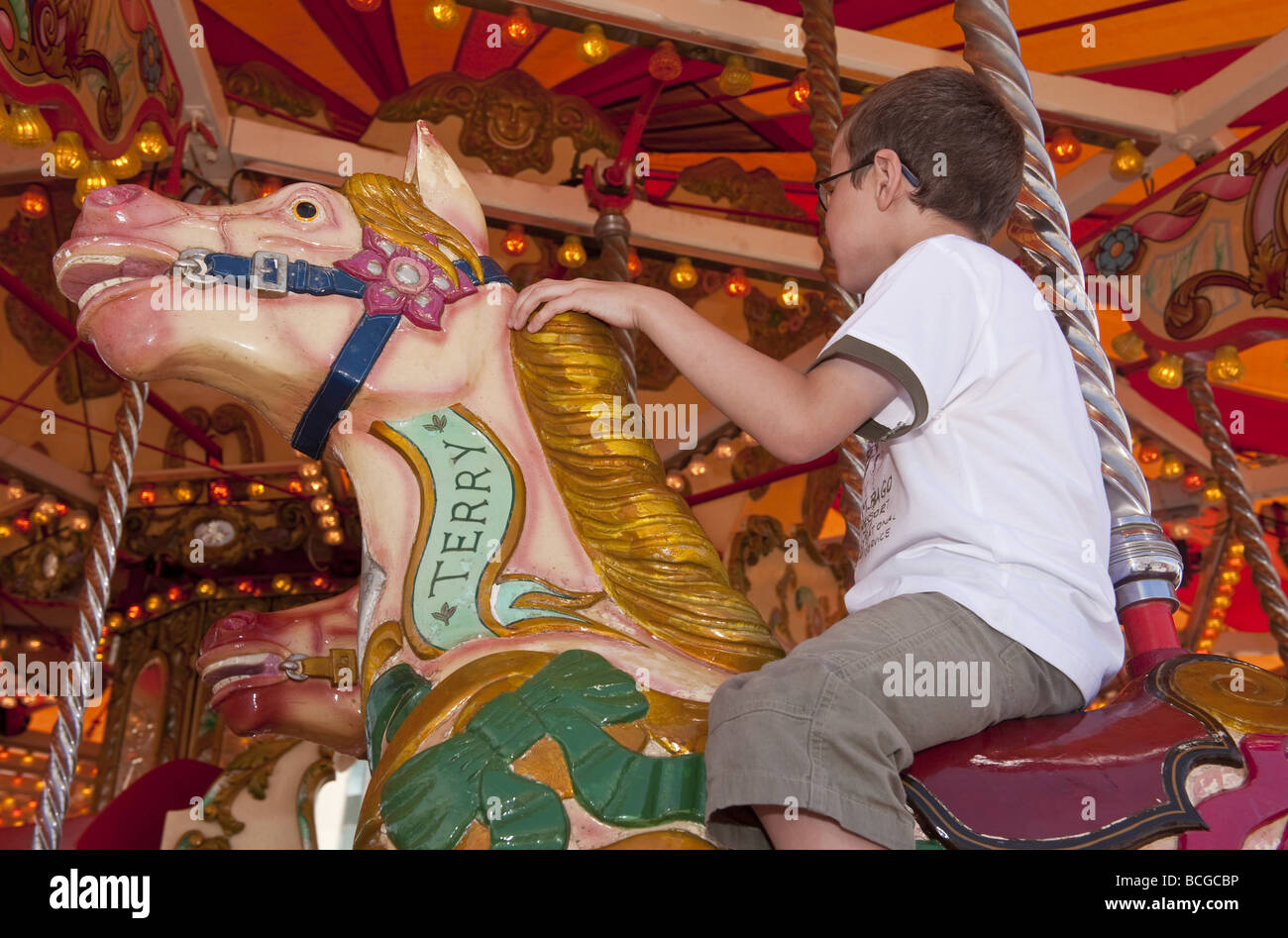 Young pre-teenage boy enjoys ride on horse on fairground carousel round about ride Stock Photo
