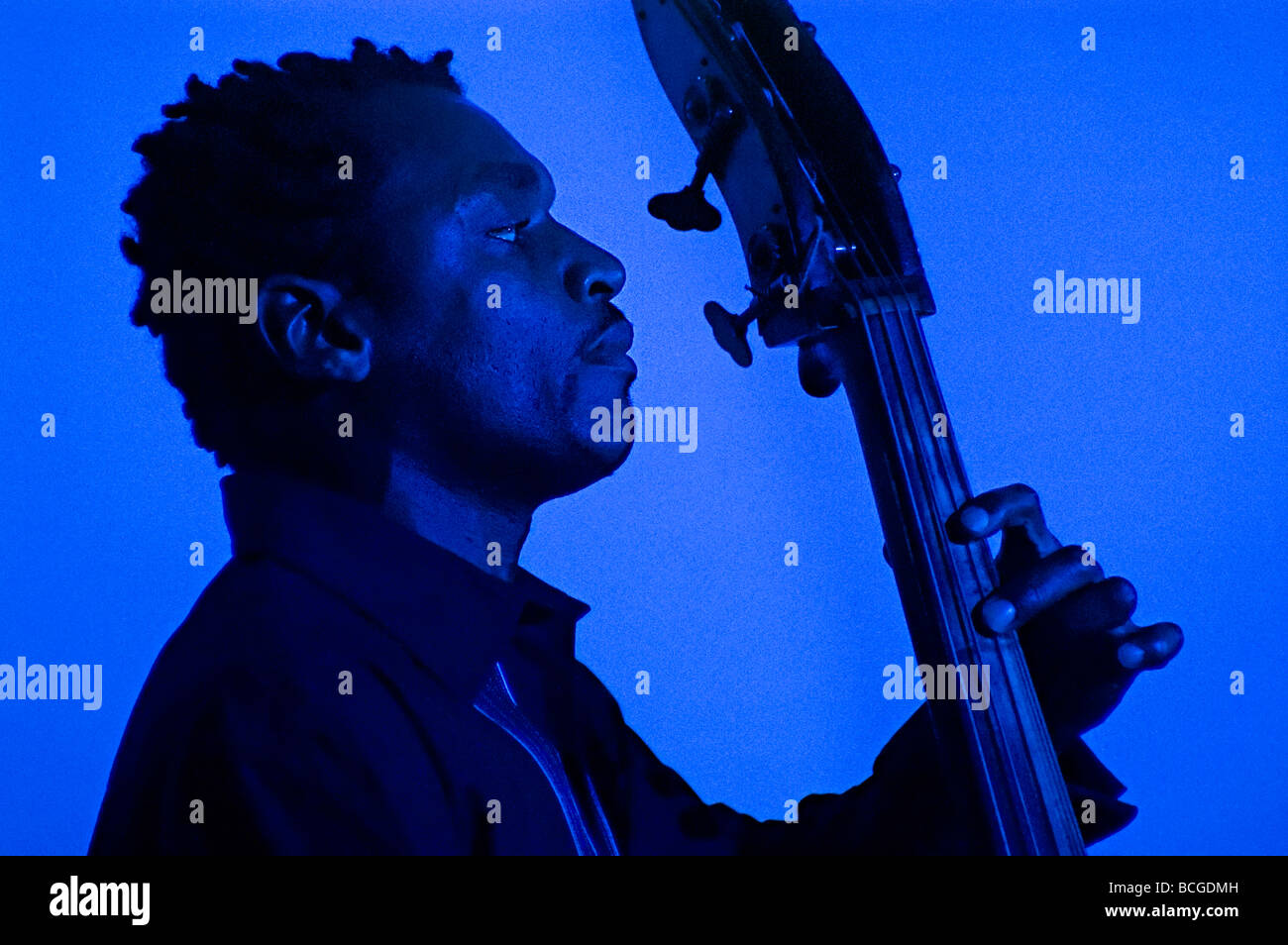 a black double bass player with shadow behind him bathed in blue light