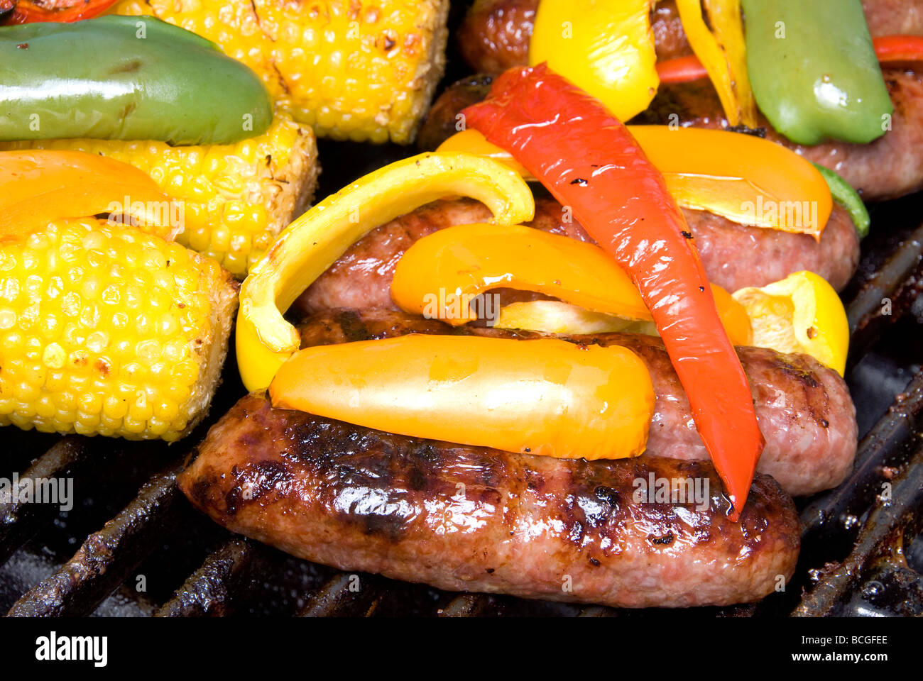 Beer bratwurst being grilled with bell peppers along with corn on the cob Stock Photo