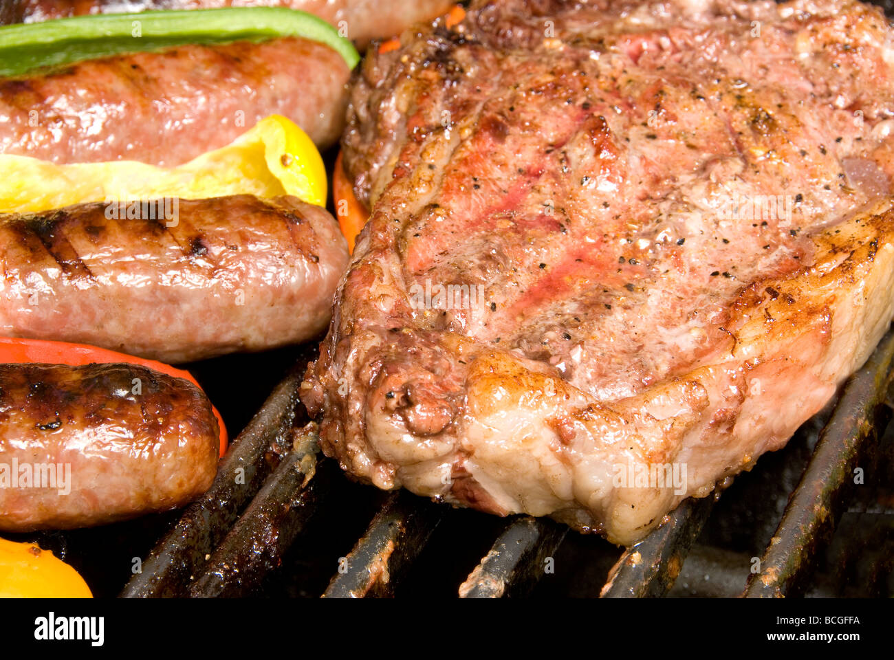 Steak and bratwurst cooming on a barbecue with bell peppers as a season and garnish Stock Photo