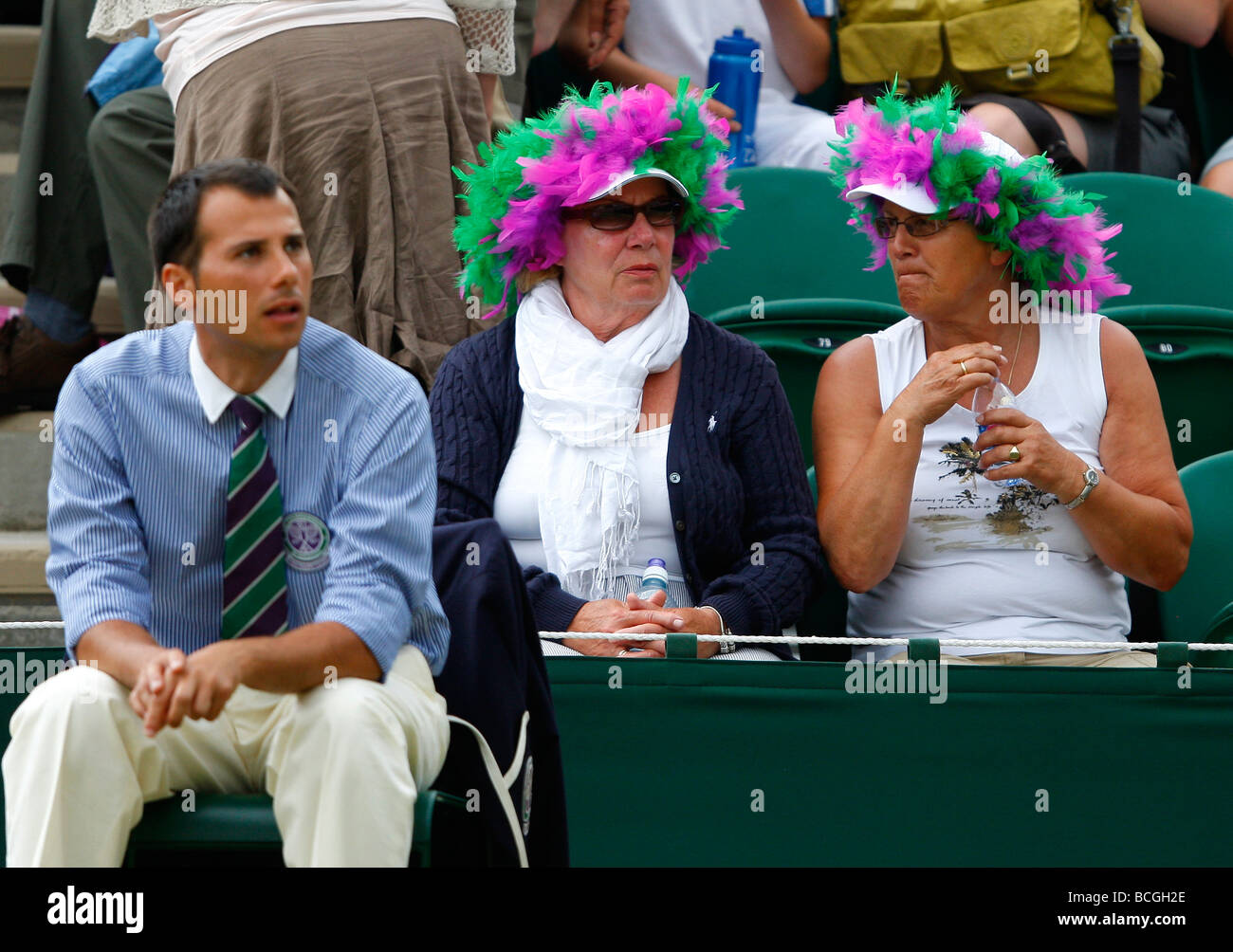 Two female spectators wearing funny hats sporting the Wimbledon colours sitting in the front row at the Championships Stock Photo