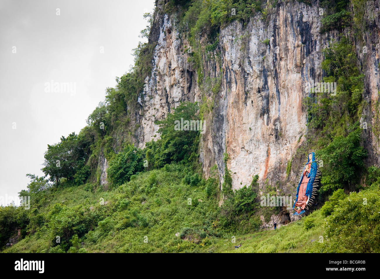 A large figure of the Vigin Mary is emblazoned upon the wall of an enormous rock face which houses a tunnel Stock Photo