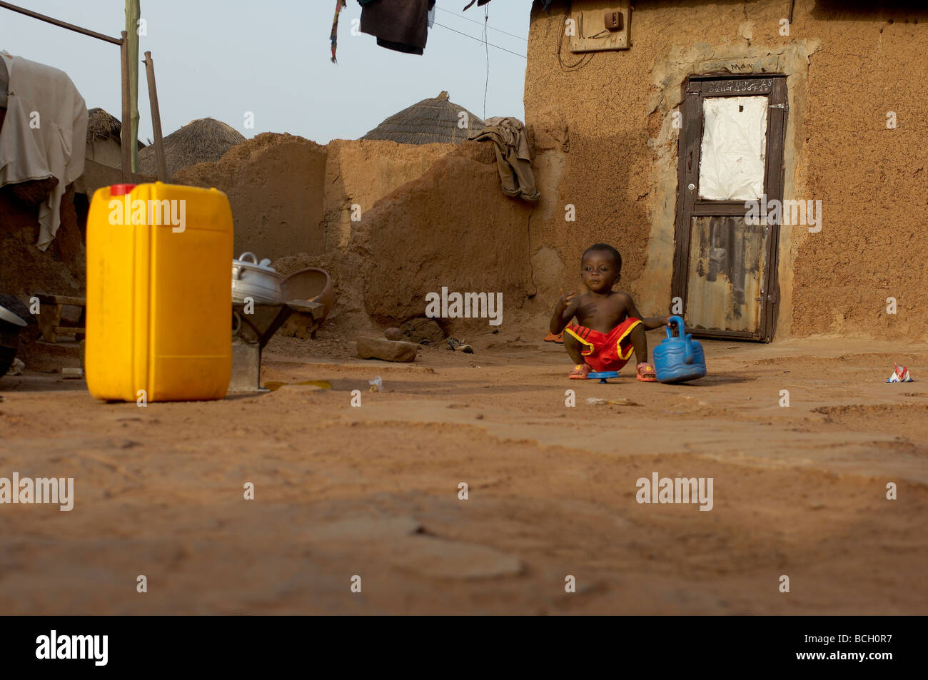 Small child on floor with blue kettle in Village in Tamale Ghana Stock Photo