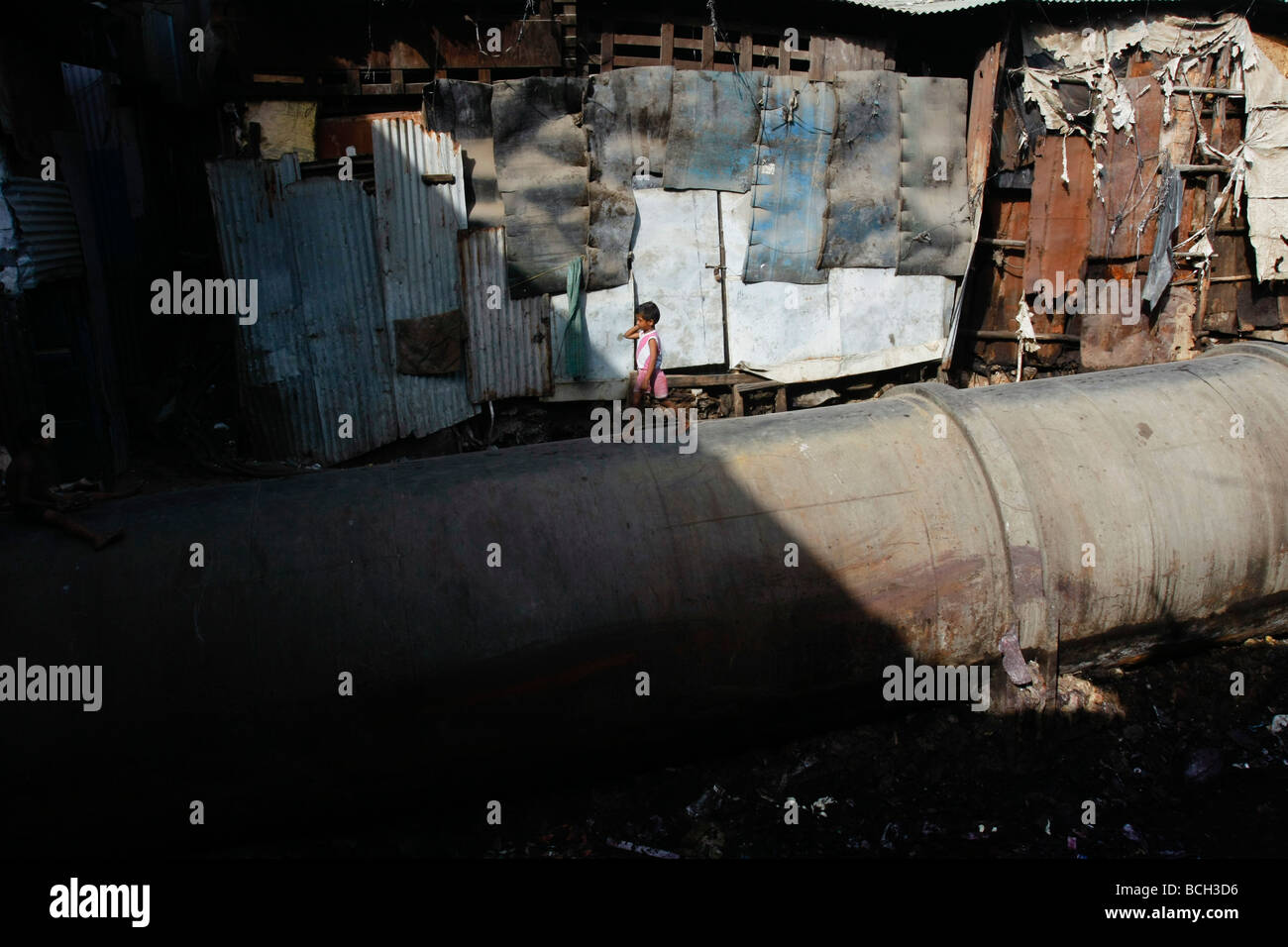 A young girl walks on a large water pipe which is used as a street in the poor slum area of Dharavi in Mumbai (Bombay) in India. Stock Photo