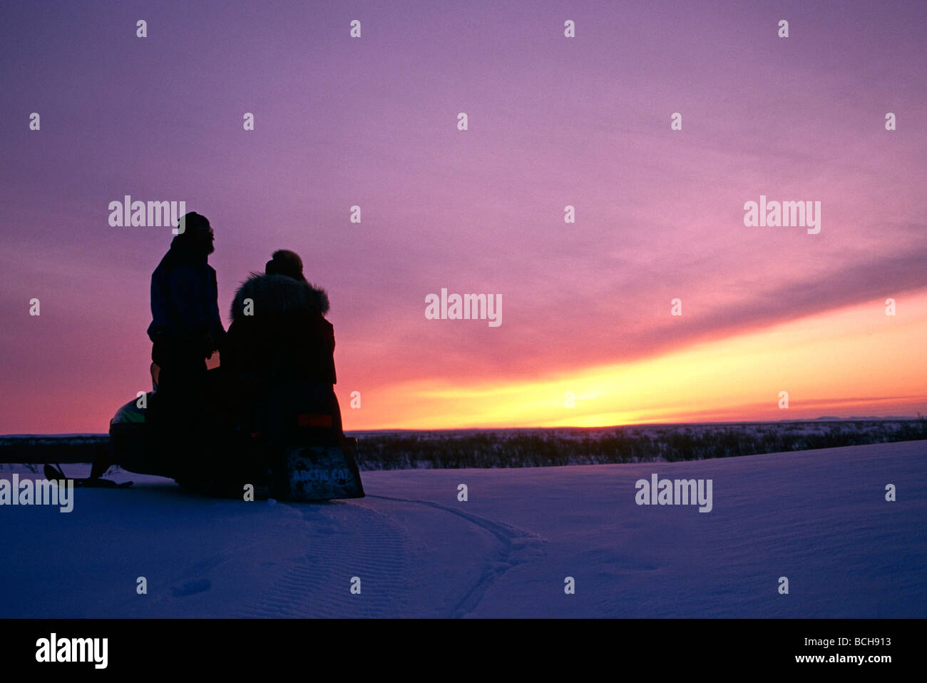 Native Couple w/Snowmobile at Sunset Stock Photo