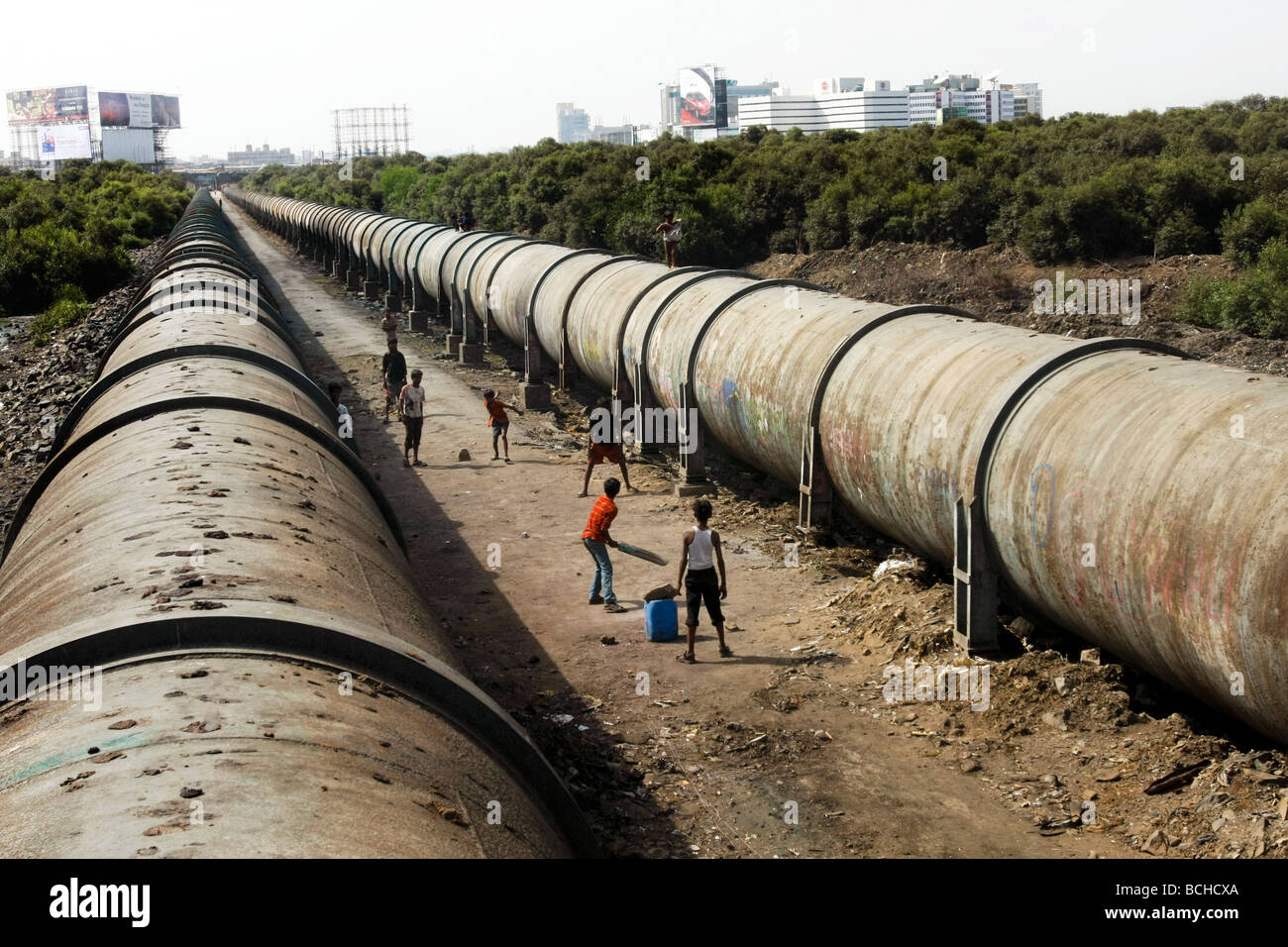Children play cricket in between two large waterpipes that runs through Dharavi, the largest slum area in Mumbai (Bombay). Stock Photo