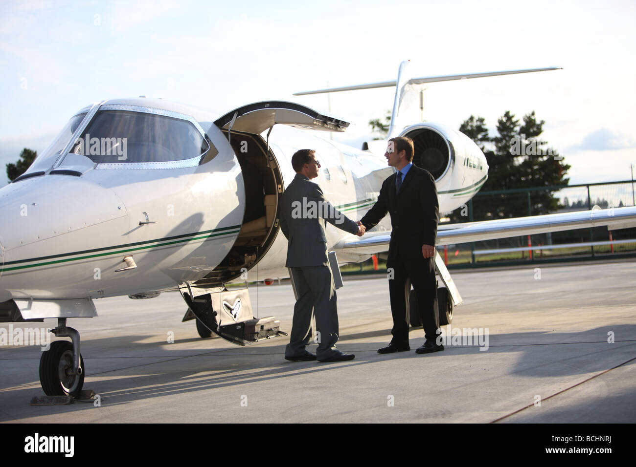 Businessmen shake hands by corporate jet Stock Photo